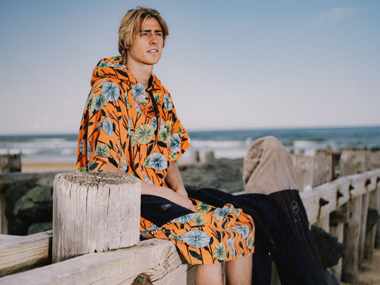 Surfeur portant un poncho de surf ALL-IN coloré au bord de l'océan