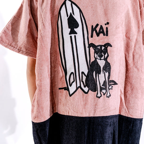 Illustration exclusive Kaï et sa planche brodée sur poncho surf junior ALL-IN Kaï Surf rose poudré