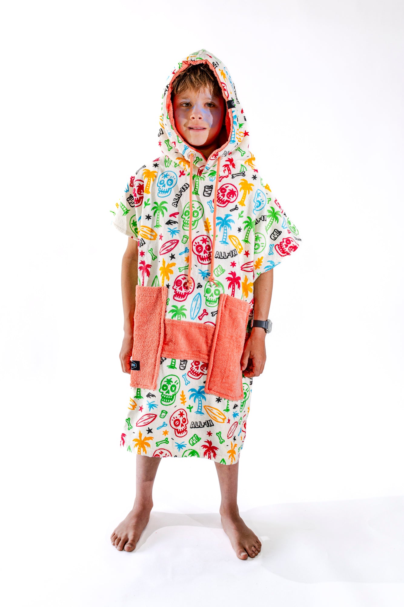 Poncho surf enfant ALL-IN Skully vue de face, motif multicolore têtes de mort et surf, poches saumon