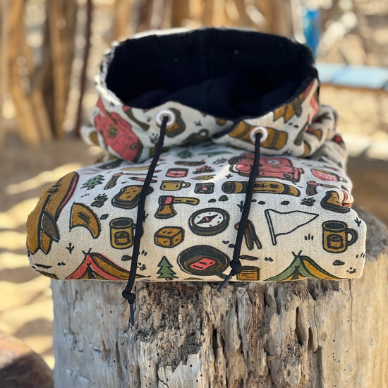 Poncho surf adulte ALL-IN Surf Camp plié sur tronc en bois, motif camping outdoor coloré, doublure capuche noire, cordon noir