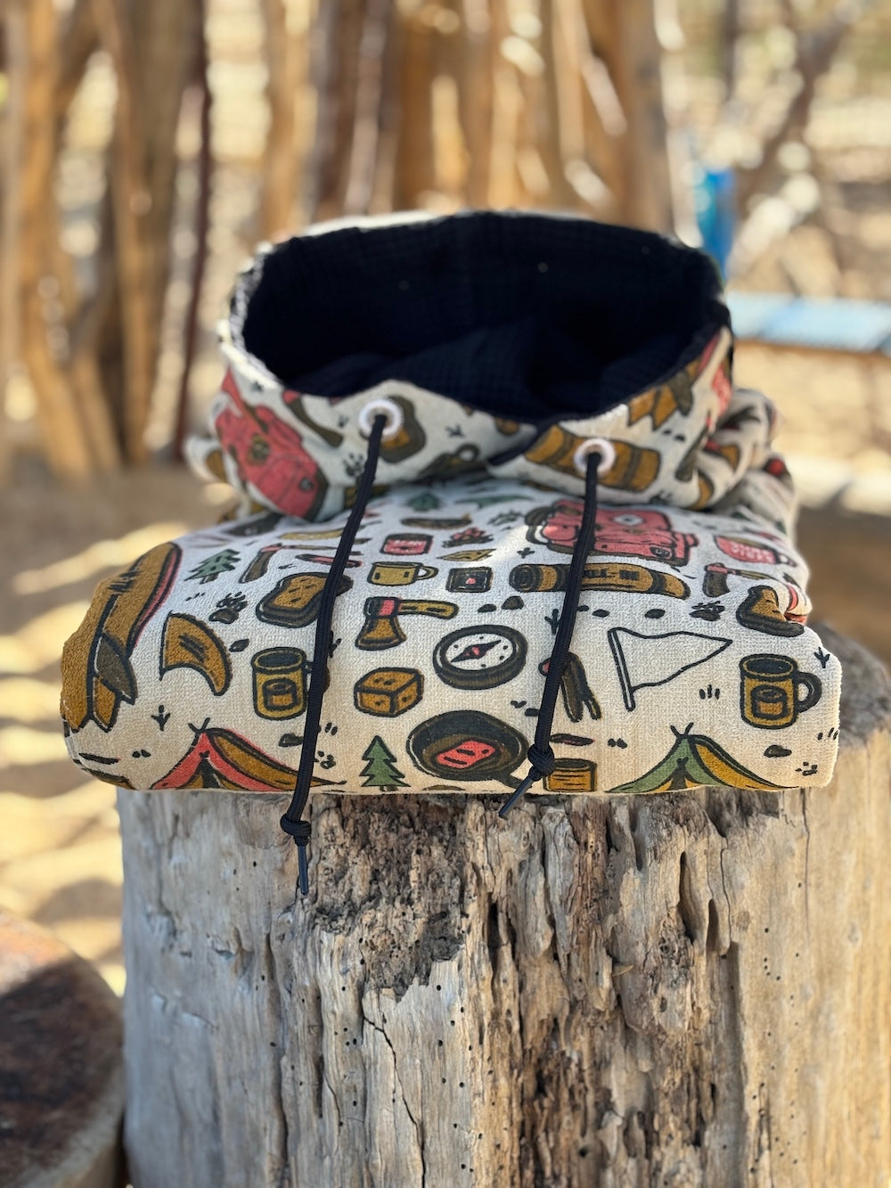 Poncho surf adulte ALL-IN Surf Camp plié sur tronc en bois, motif camping outdoor coloré, doublure capuche noire, cordon noir