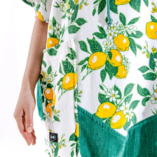 Poncho surf femme ALL-IN Lemonade vue de face, motif citrons jaunes sur fond blanc, poches vertes