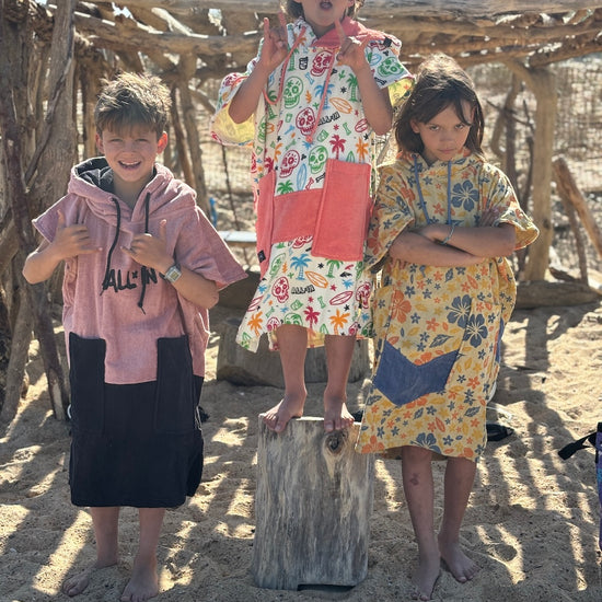 Enfants portant des ponchos surf ALL-IN Flore sur la plage, motif floral jaune et orange