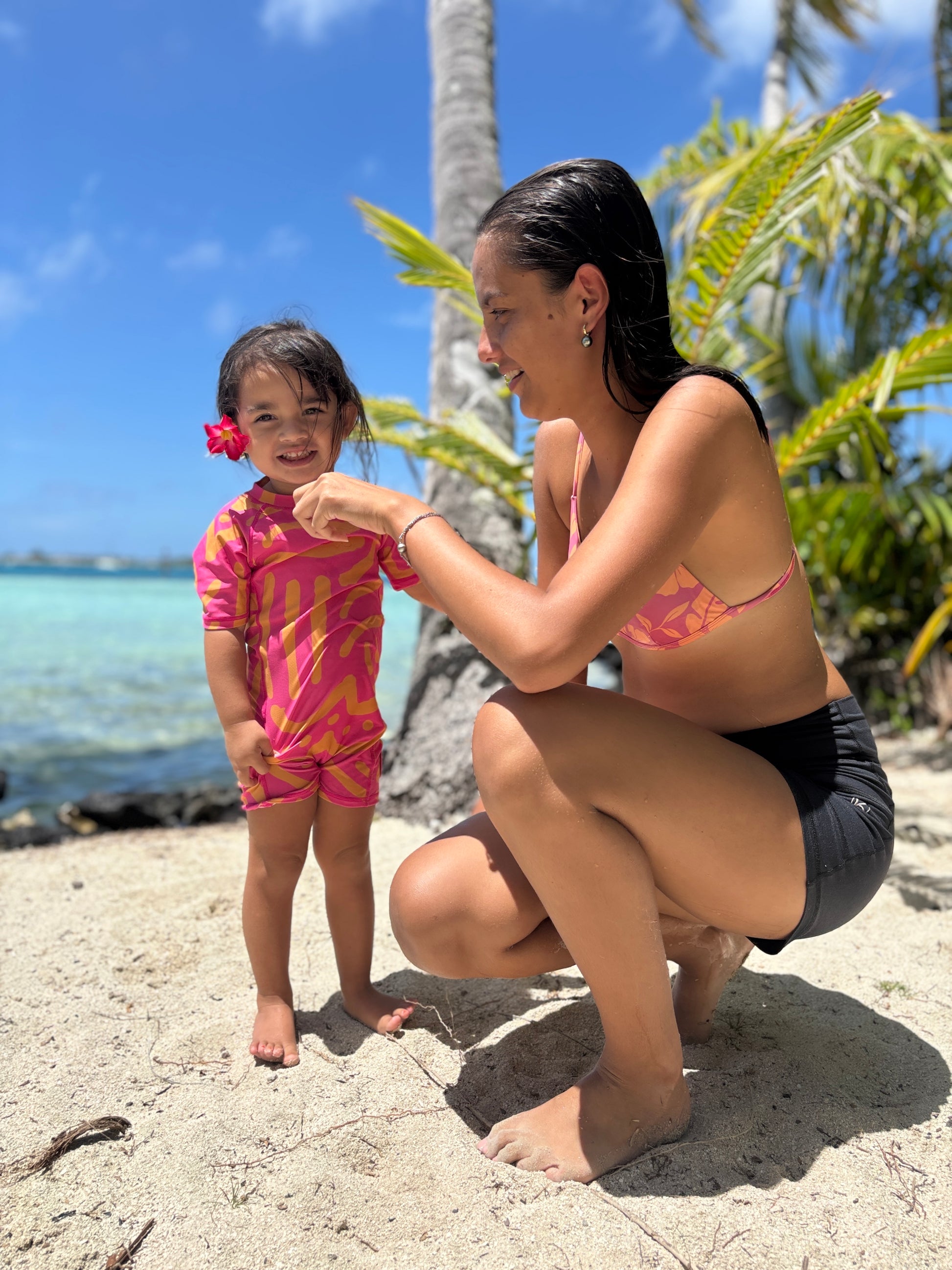 Petite fille portant la combinaison anti-UV ALL-IN Matis Rose sur une plage tropicale avec sa maman