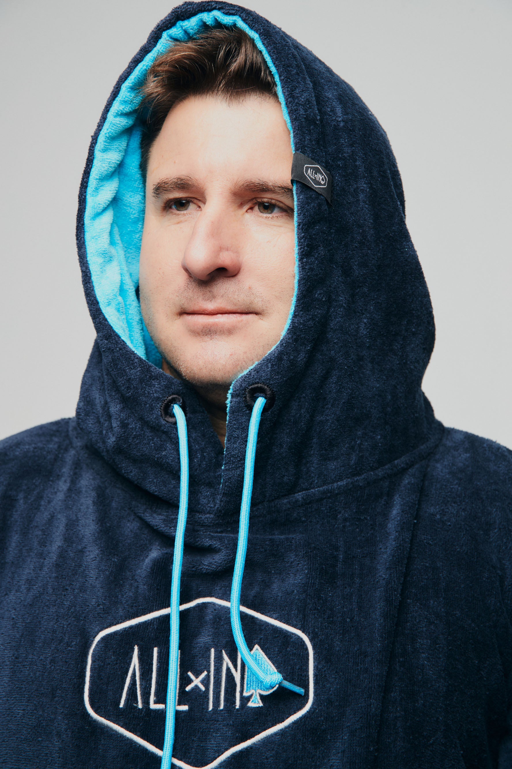 Gros plan sur la capuche doublée turquoise et le logo ALL-IN brodé du poncho de surf Blue Surf