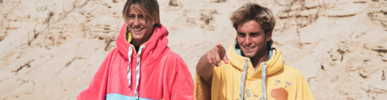 Two young surfers in ponchos on the beach